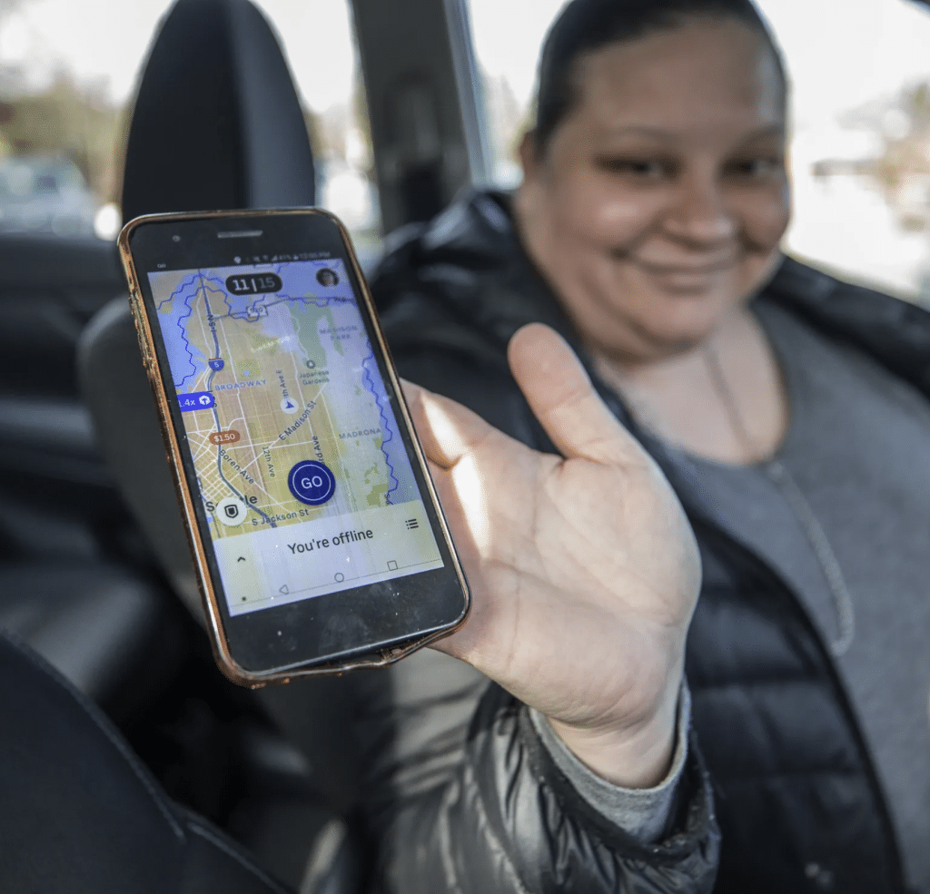 Gig worker holding up phone app in car